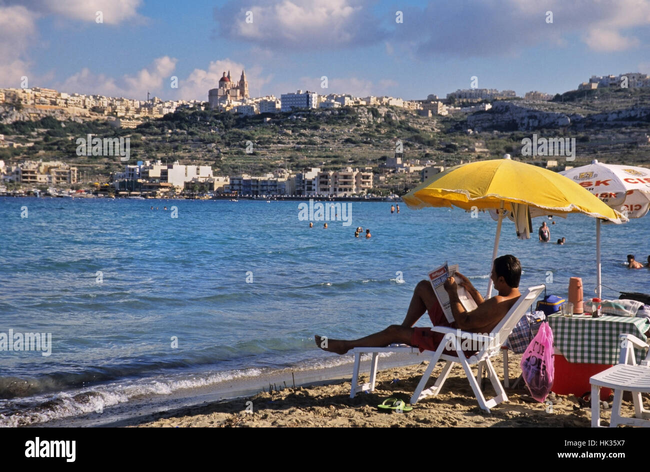 L'uomo distendersi leggendo il giornale, spiaggia di Mellieha, Malta Foto Stock
