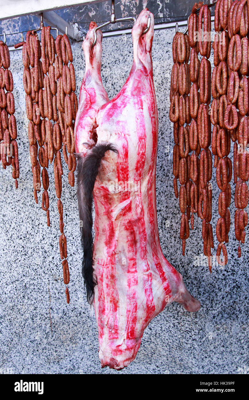 Crudo fresco pelato con la carne di maiale e salsicce appeso nella parte anteriore del negozio di macellaio sulle strade del centro cittadino del Cairo in Egitto Foto Stock