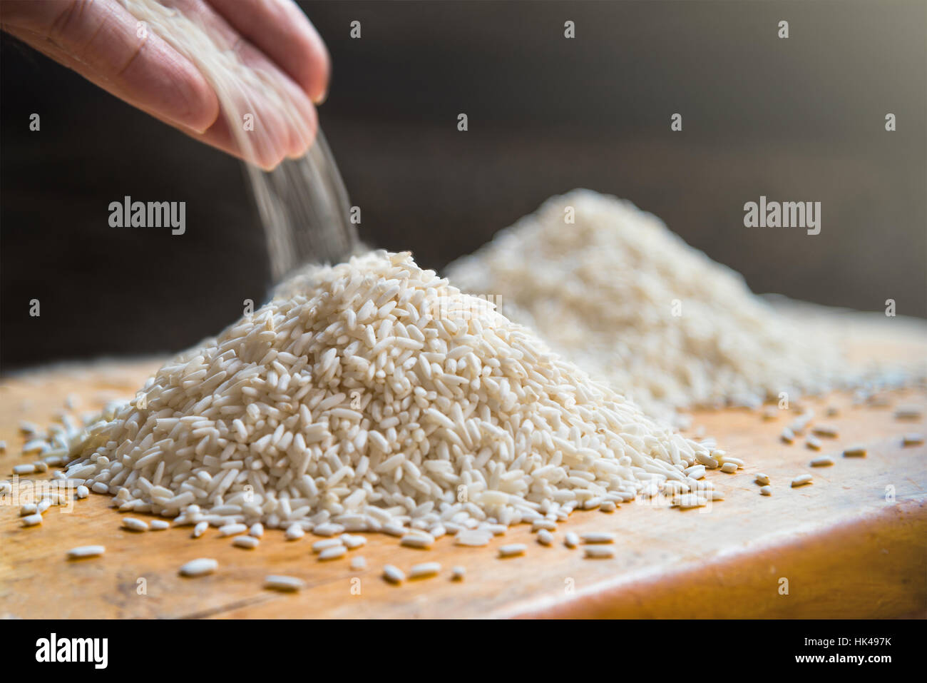Versa manualmente il riso sulla pila di riso in bianco sul tavolo di legno sfondo, metafora ingrediente, nutrizione, carboidrato cibo concetto, il fuoco selettivo Foto Stock