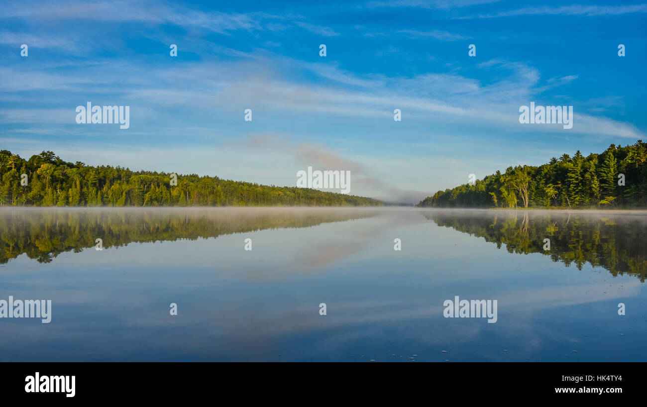 Luminose a metà estate cielo blu, foschia mattutina nel mezzo del lago Corry. Acqua calda e lo scambiatore di calore aria allo spuntar del giorno crea misty patch lungo il litorale. Foto Stock