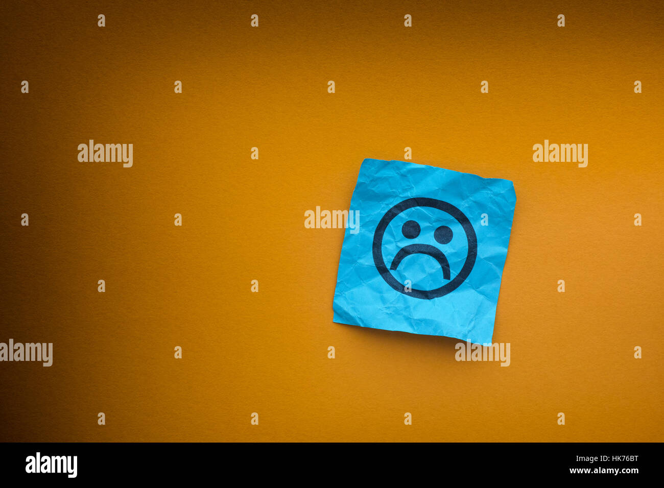 Carta blu nota con la faccia triste su una carta gialla sfondo. Concetto di depressione. Foto Stock