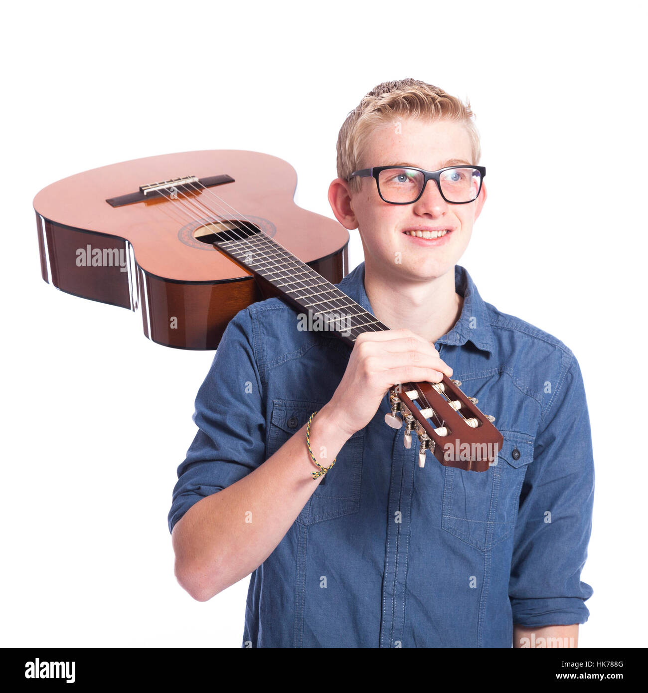 Caucasian teen boy in blu porta gli occhiali e porta la chitarra classica sulla spalla in studio contro uno sfondo bianco Foto Stock