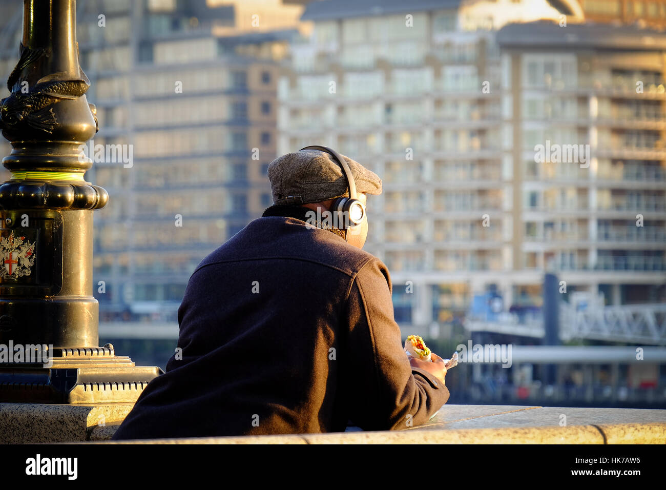 Un uomo che indossa le cuffie mangia il suo pranzo e si affaccia sul Fiume Tamigi Foto Stock