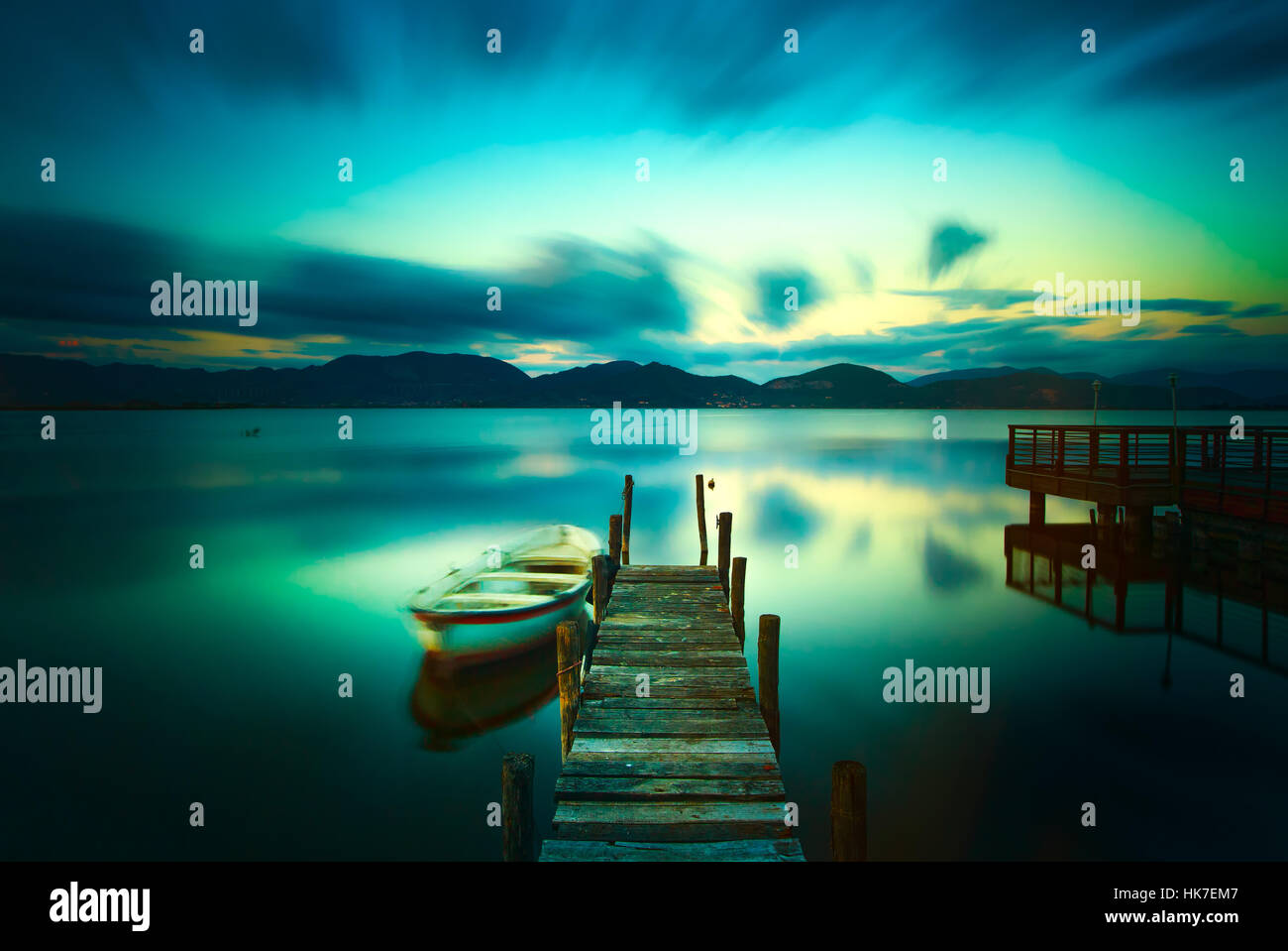 Il molo di legno o un pontile e una barca sul lago tramonto Cielo e acqua di riflessione. Una lunga esposizione, Versilia Massaciuccoli, Toscana, Italia. Foto Stock