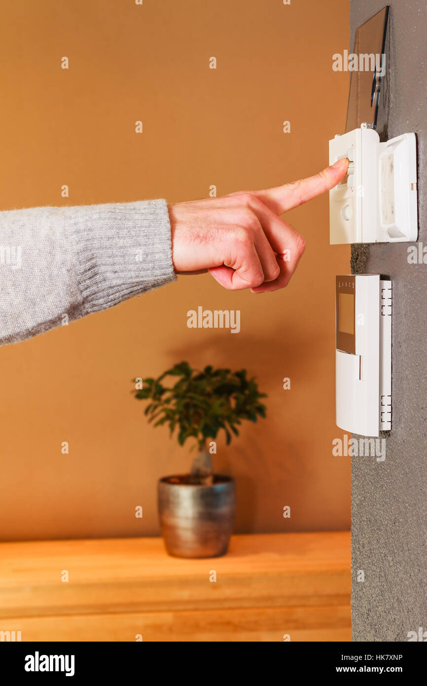 Giovane Maschio lato premendo il pulsante di apparecchio elettronico su parete di casa moderna. Pulire scena di sfondo grigio maglione di lana. Foto Stock