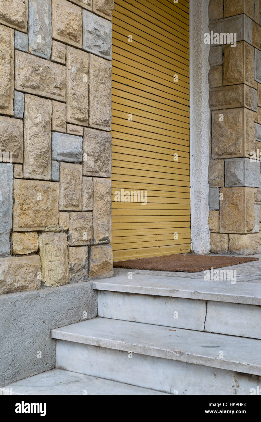 Angolo di visualizzazione di mattoni di pietra colorata, muro bianco tre gradini in marmo e chiusa gialla verticale porta rullo Foto Stock