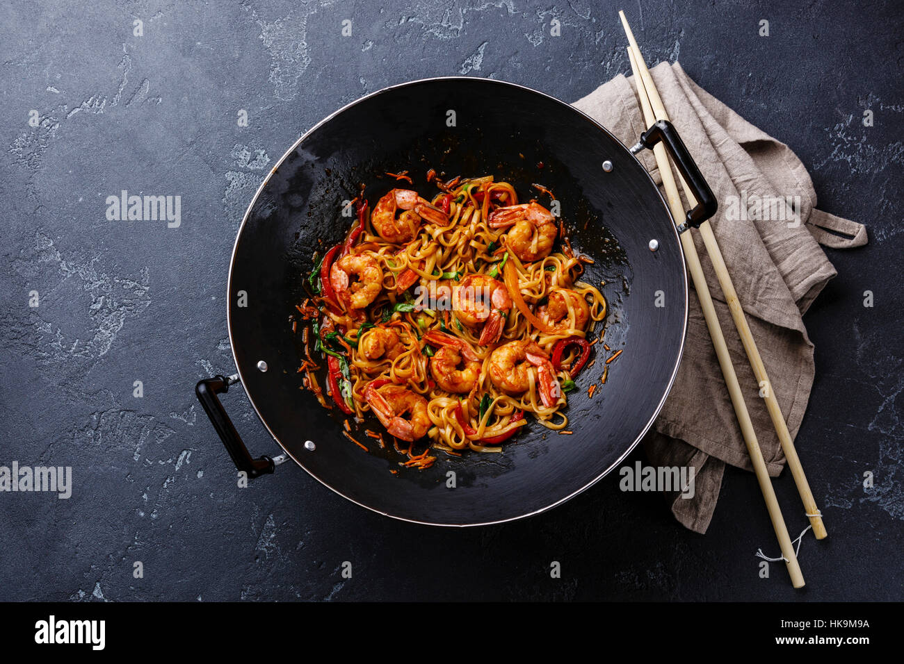 Udon friggere gli spaghetti con i gamberi nel wok padella in pietra scura sullo sfondo Foto Stock