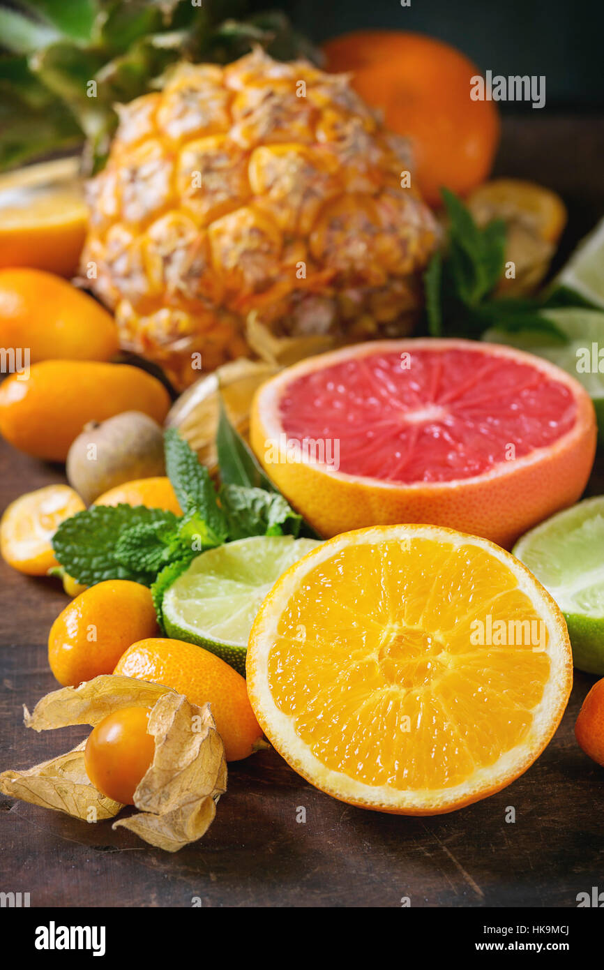 Varietà di interi e fette di agrumi ananas, pompelmo, limone, calce, kumquat, clementina e physalis con la menta su legno scuro dello sfondo. Foto Stock