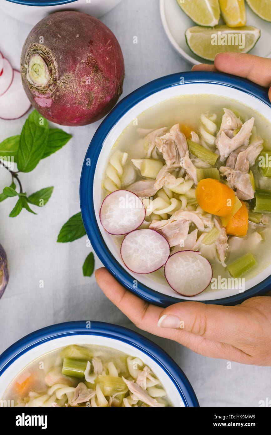 Mani tenendo una ciotola di zuppa di pollo con pasta, porri e carote. Foto Stock