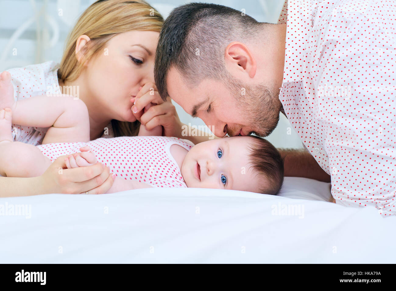 Bambino con i suoi genitori casa felice sul lettino. Mamma e papà kiss Foto Stock