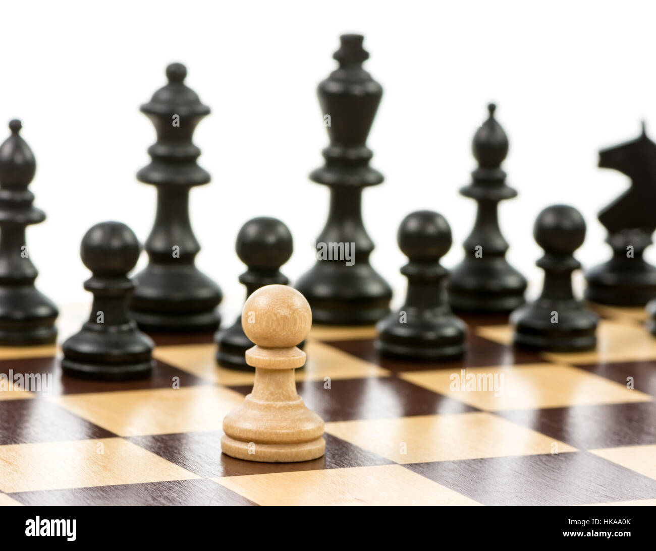 Pedone bianco contro una superiorità del nero di pezzi di scacchi su una scacchiera. Messa a fuoco selettiva. Foto Stock