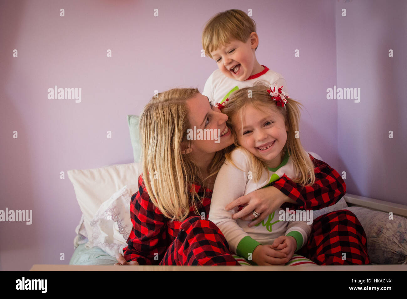 Amorevole Madre snuggling con il figlio e la figlia sul letto indossando pigiami di natale Foto Stock