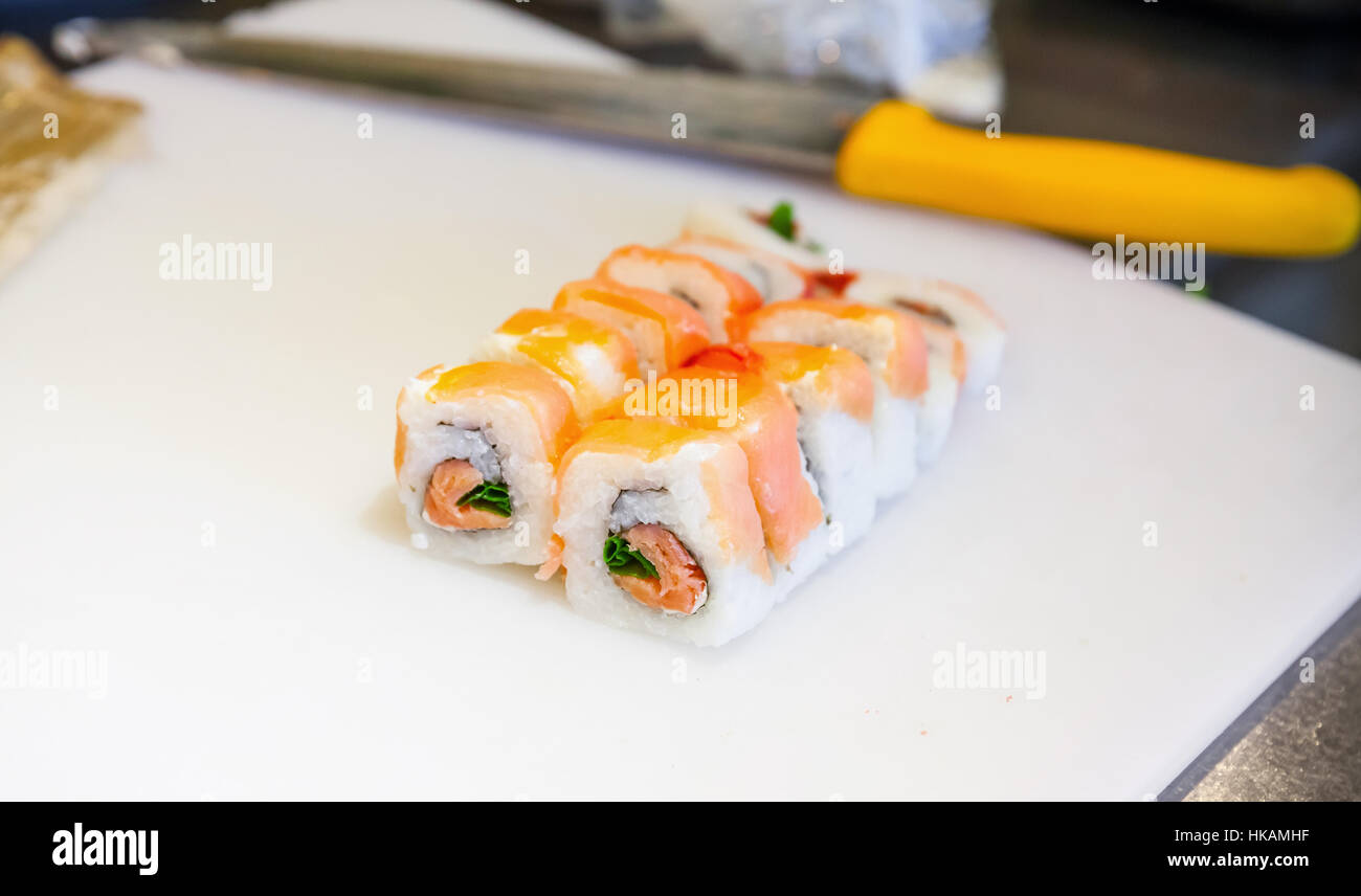 Il sushi tradizionale Giapponese rotoli con salmone laici bianco sul tagliere con il capo di coltello. Primo piano con il fuoco selettivo Foto Stock