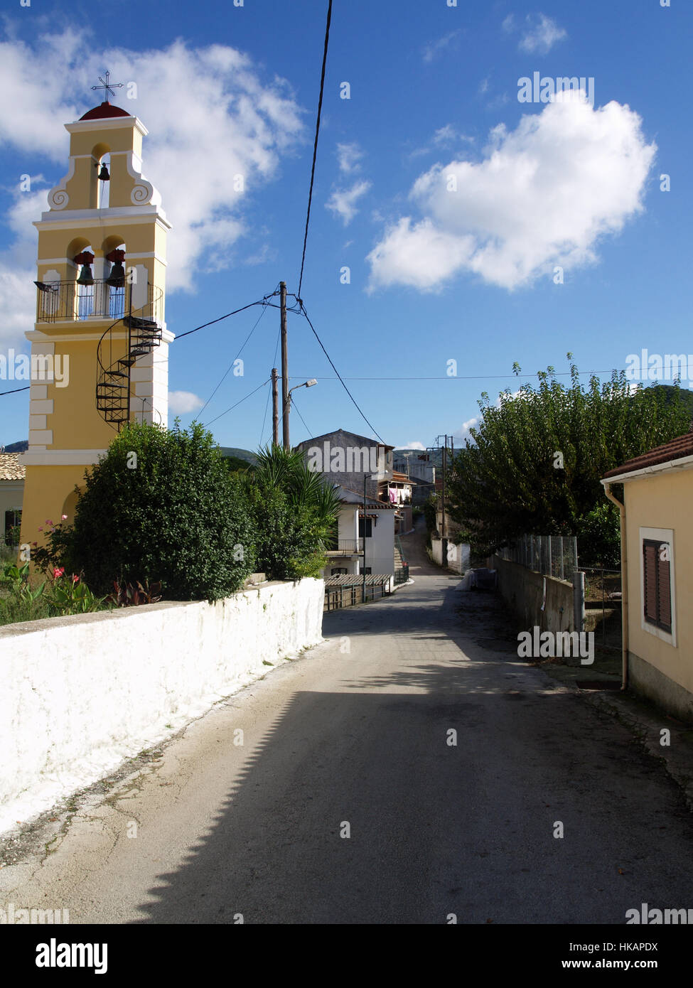 La strada principale che attraversa il villaggio di Pagi, l'isola di Corfù, Grecia con torre campanaria a sinistra Foto Stock