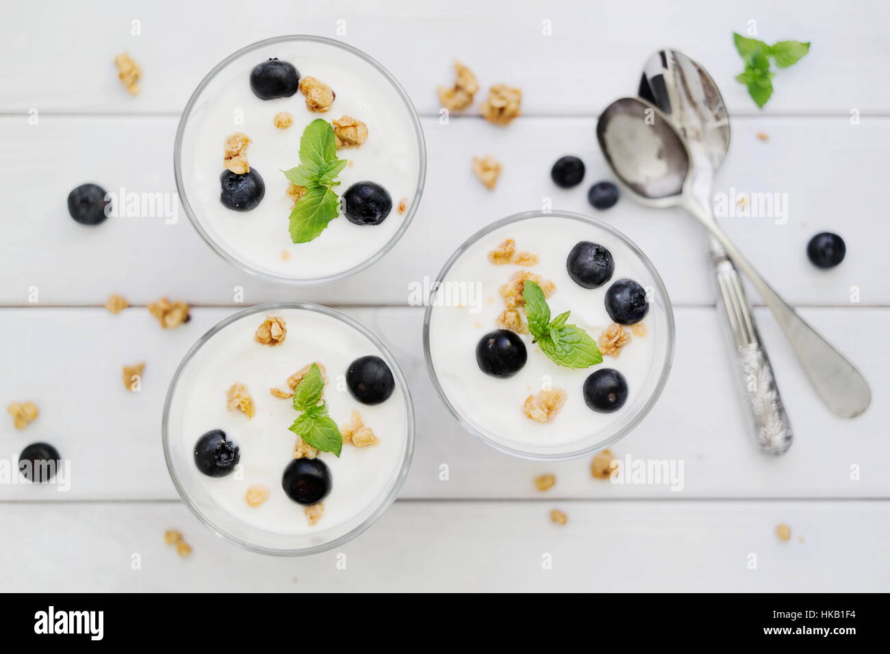 Deliziosi dessert fatti in casa di muesli e mirtillo yogurt parfait di vetro con la menta su bianco di pannelli di legno. Concetto di dessert leggero. Vista dall'alto in basso. Foto Stock