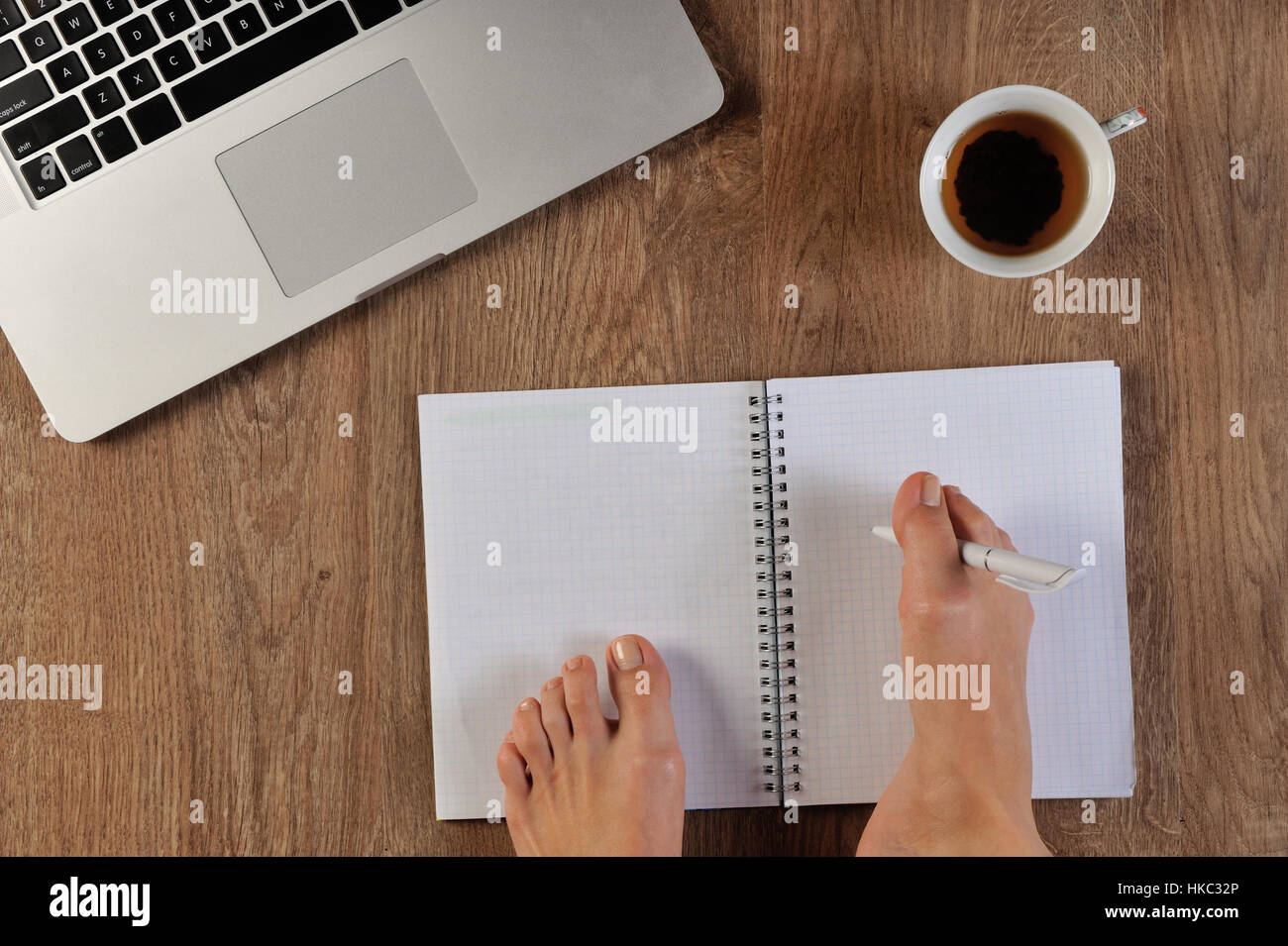 Disattivare la persona scrivendo con piede in notebook infront di laptop Foto Stock