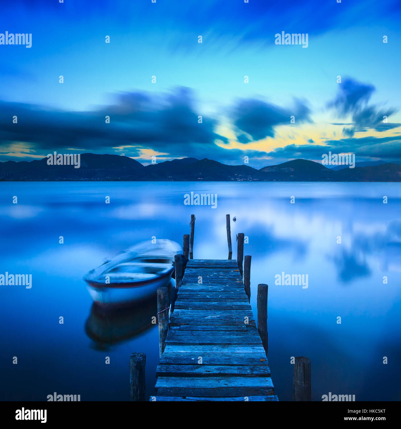 Il molo di legno o un pontile e una barca sul lago tramonto Cielo e acqua di riflessione. Una lunga esposizione, Versilia Massaciuccoli, Toscana, Italia. Foto Stock