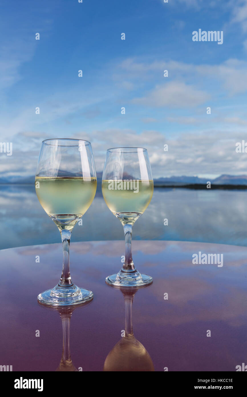 Due bicchieri di vino riempito con vino bianco riflettono su un piano di un tavolo accanto al lago Tikchik, Wood-Tikchik State Park, Southwestern Alaska, STATI UNITI D'AMERICA Foto Stock
