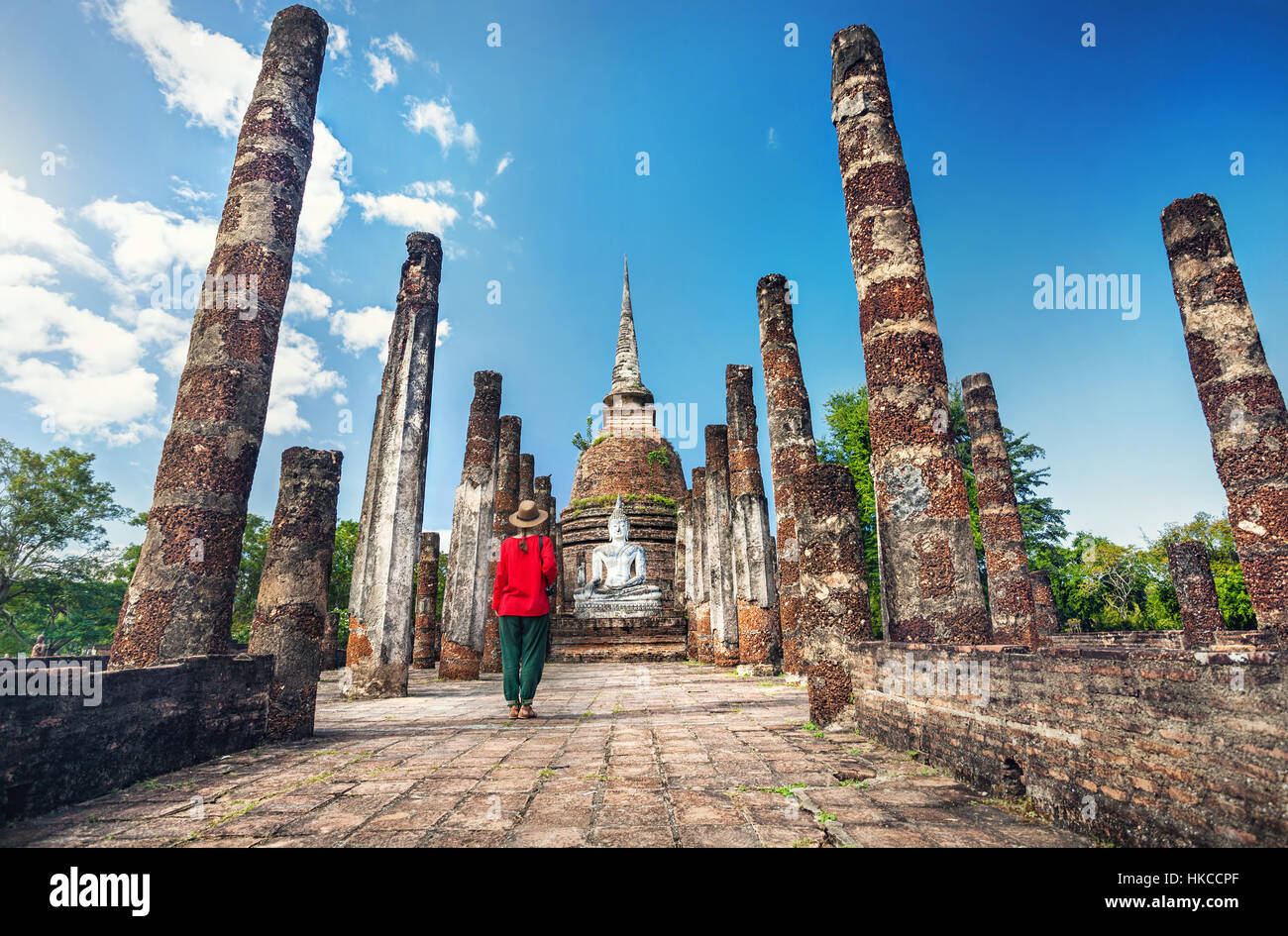 Tourist donna in costume rosso guardando antica statua di Buddha nel Wat Sa Si di Sukhothai Historical Park, Thailandia Foto Stock