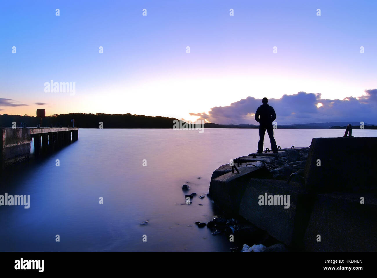 Uomo in piedi da soli che si affacciava su un lago verso un tramonto Foto Stock