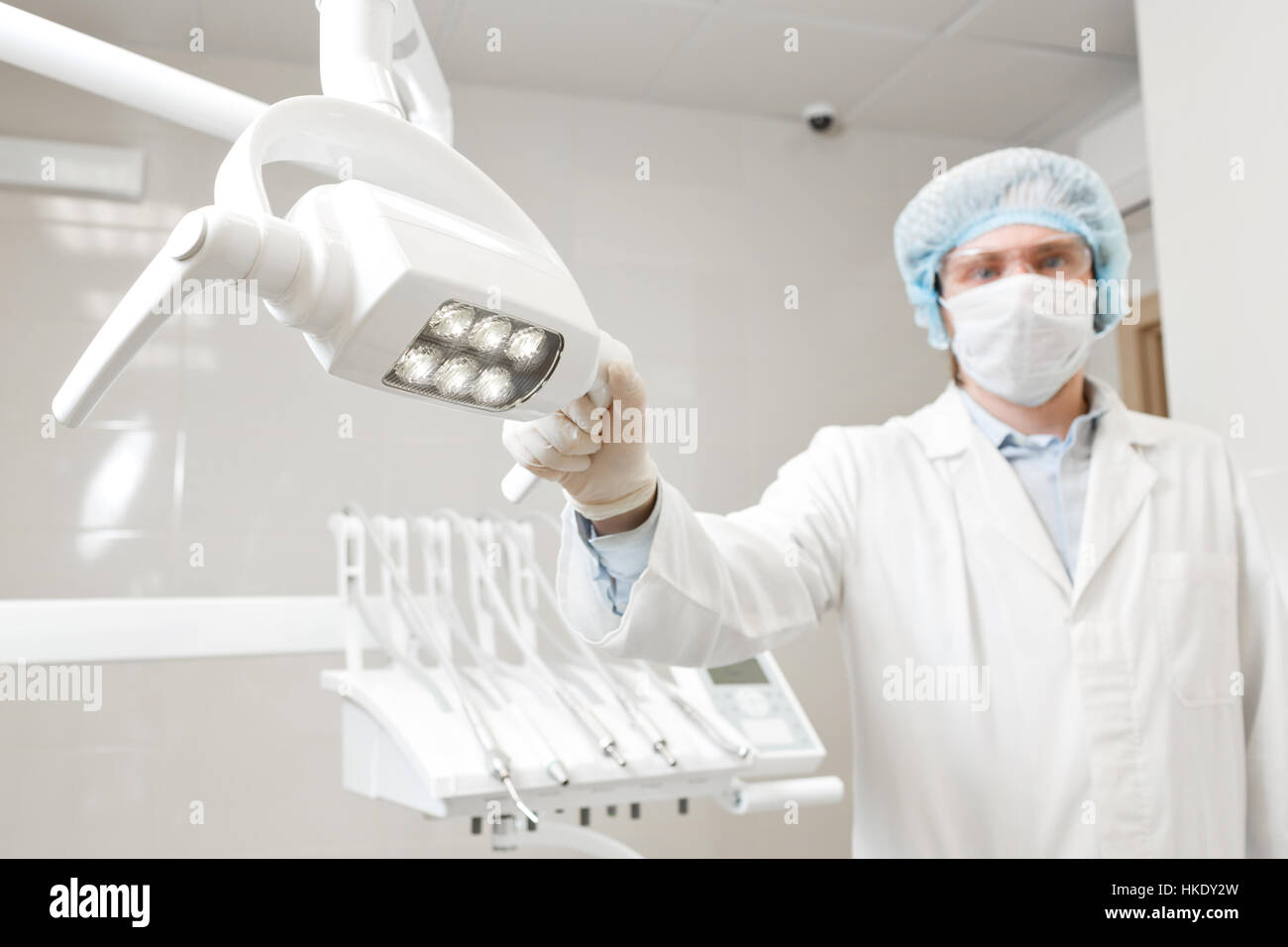 Vista dal basso di un ritratto di medico dentista, chirurgo in uniforme e la maschera sul suo volto, indossando occhiali, tenendo la lampada nella sua mano. Foto Stock