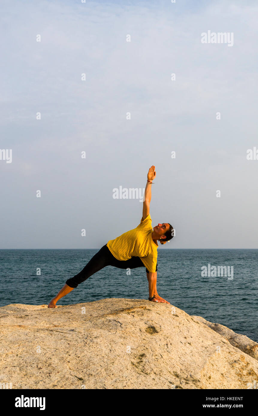 Una giovane donna è mettere in pratica la posizione Utthita-Parshvakonasana su una roccia sul mare Foto Stock