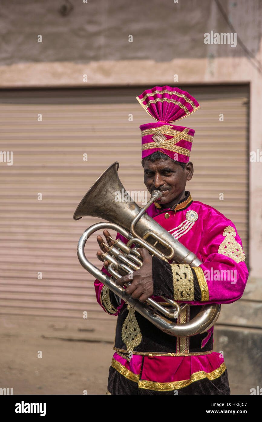 Un suonatore di corno vestito in un coloratissimo corteo vestito in un matrimonio indiano. Foto Stock