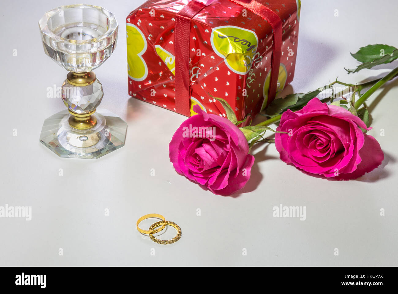 Romantico rose rosa con avvolto articolo regalo cristallo stand di candela e gli anelli di nozze isolato in uno sfondo bianco. Foto Stock