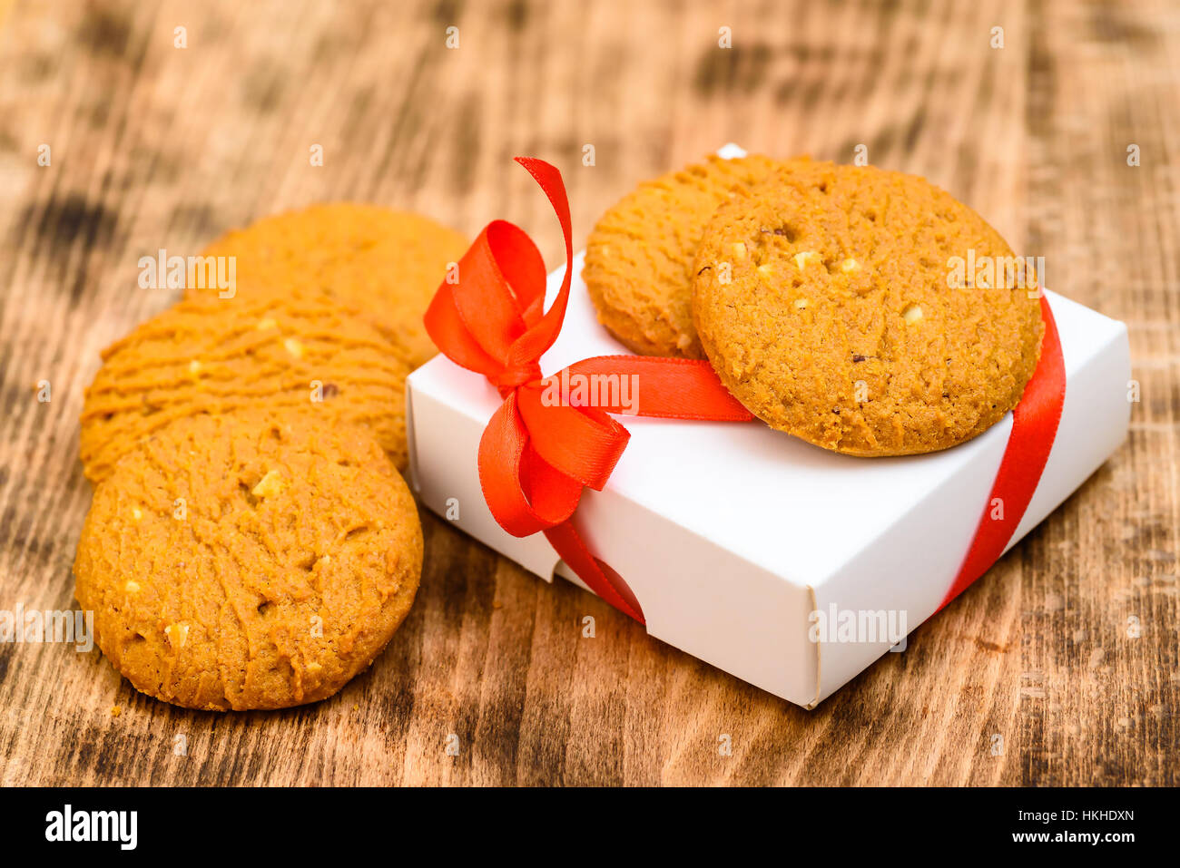 Piccolo presente di colore bianco con fiocco rosso a fianco e sotto i cookie sul vassoio in legno Foto Stock