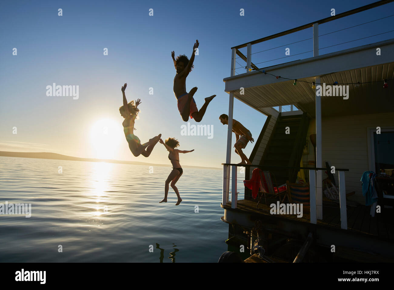 Giovani amici adulti salta fuori estate houseboat in oceano al tramonto Foto Stock