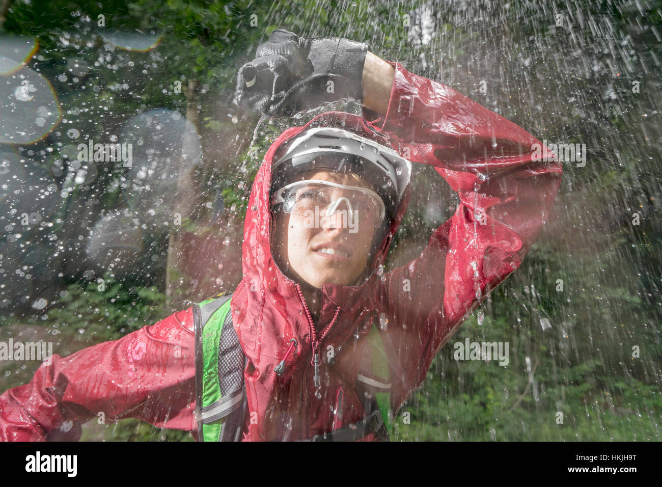 Mountainbiker in piedi sotto la pioggia con la mano sopra la testa, Kampenwand, Baviera, Germania Foto Stock