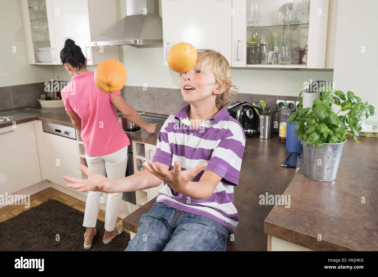 Ragazzo giocoleria con arance mentre madre preparare cibi,Baviera,Germania Foto Stock