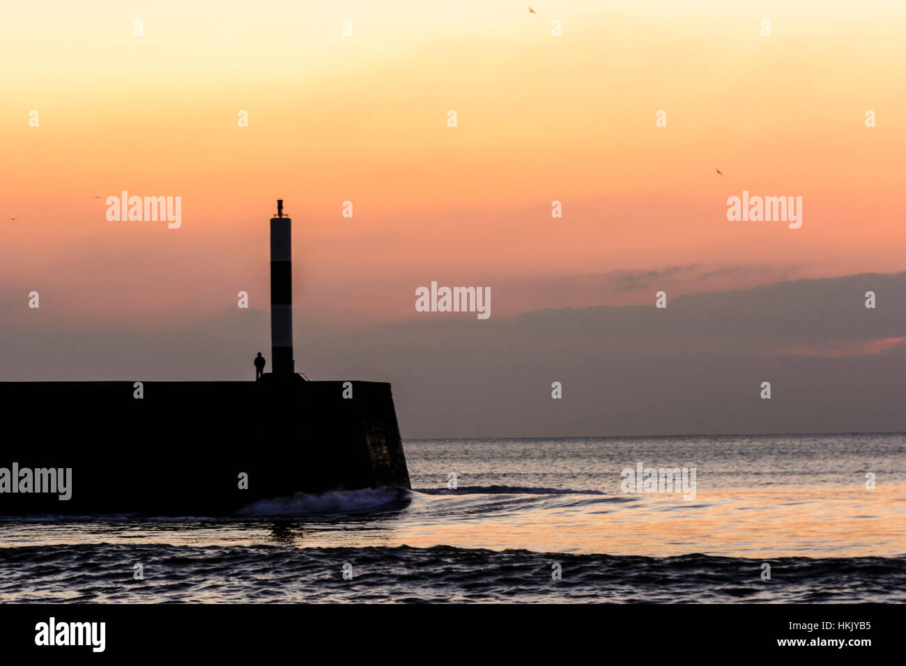 Un giovane uomo che guarda al mare al tramonto in Aberystwyth, Galles Foto Stock