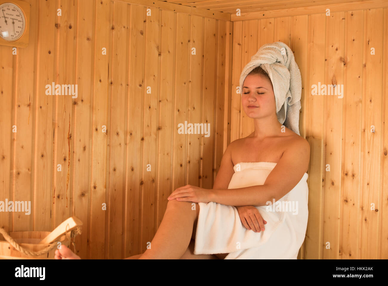 Giovane donna bionda in sauna in legno con asciugamano sul suo capo Foto Stock