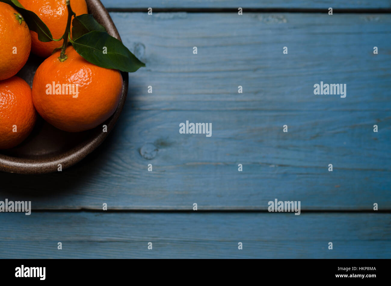 Una ciotola di clementine fresche blu su uno sfondo di legno con una stanza per il testo Foto Stock