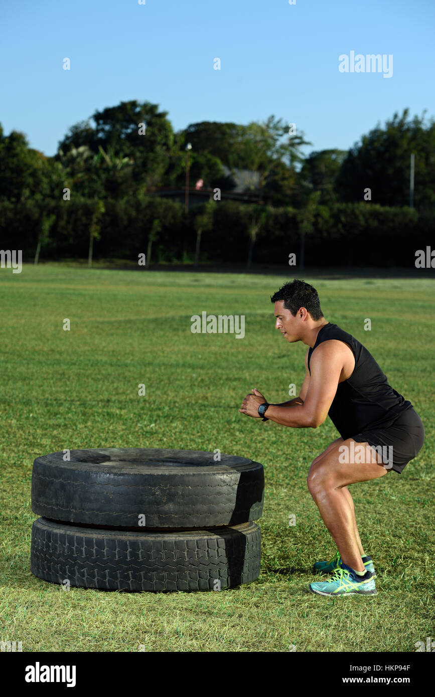 Uomo allenamento facendo saltare sul pneumatico su erba dello stadio Foto Stock