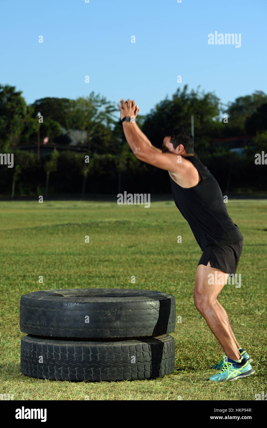 Sport uomo cominciano a saltare sul pneumatico in erba verde park Foto Stock