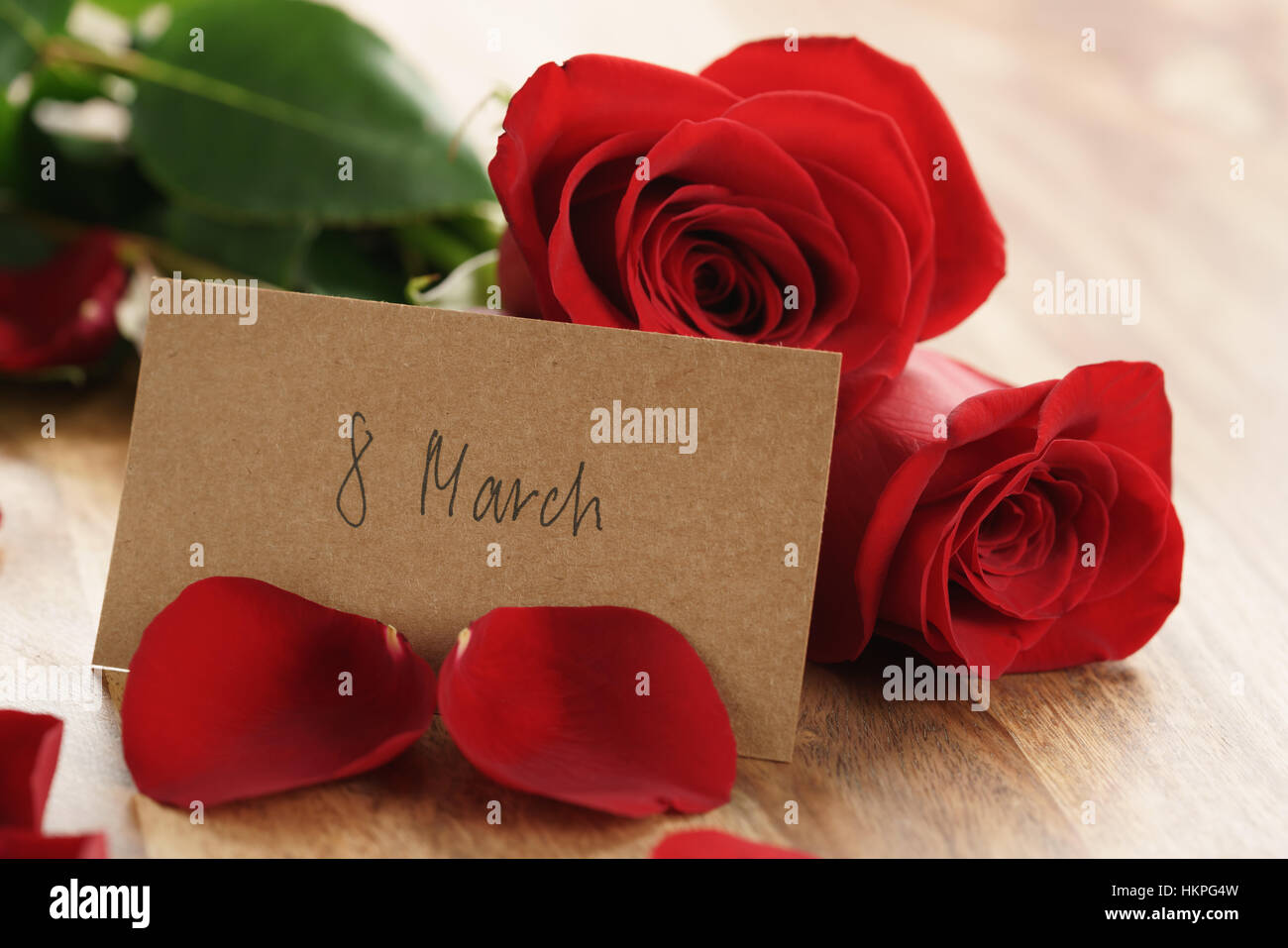 Tre rose rosse e petali di fiori sul vecchio tavolo in legno con 8 marzo scheda carta Foto Stock