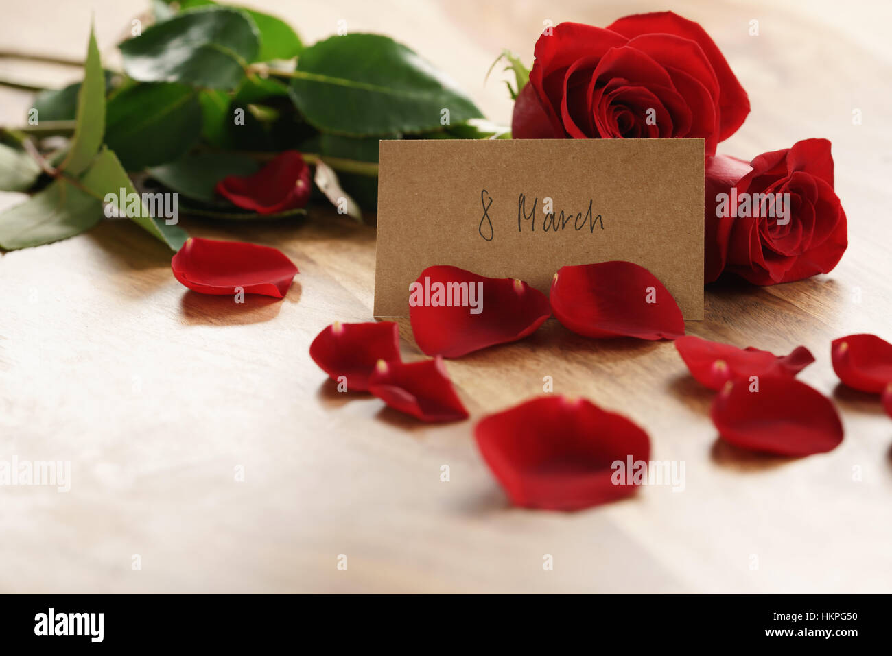 Tre rose rosse e petali di fiori sul vecchio tavolo in legno con 8 marzo scheda carta Foto Stock