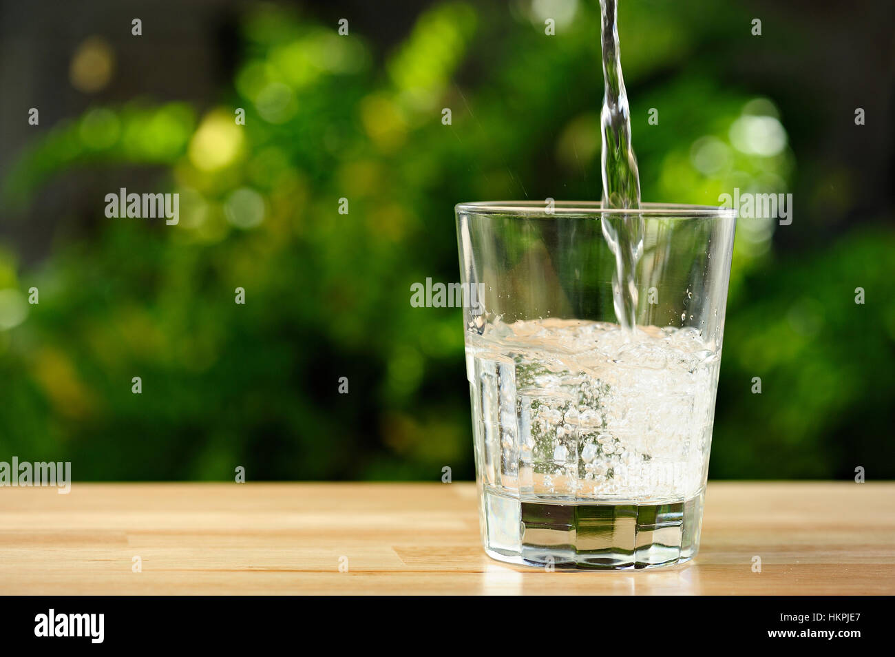 Versando acqua trasparente in vetro trasparente in giardino verde Foto Stock