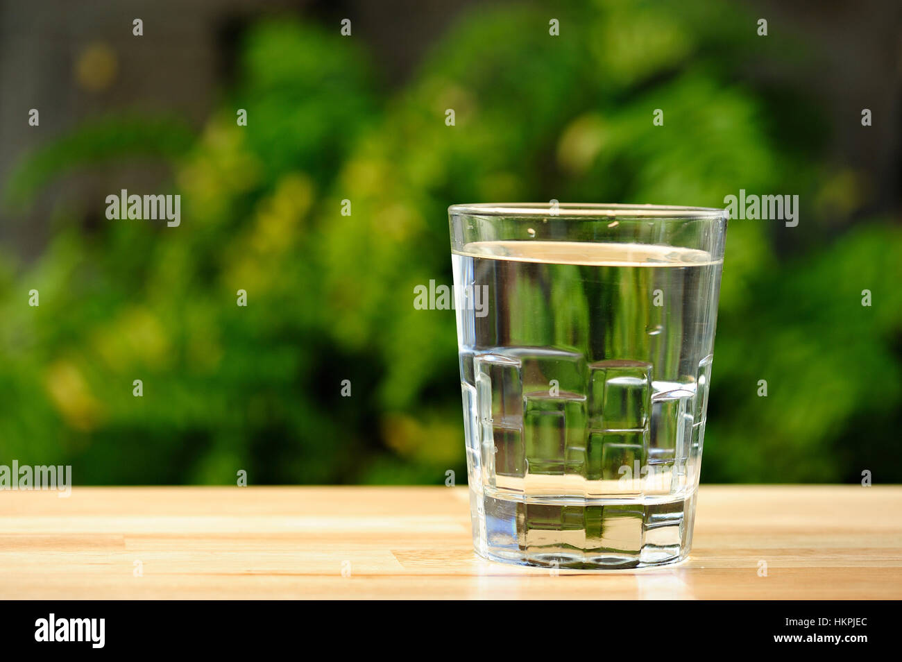 Bicchiere pieno di acqua in giardino verde sullo sfondo Foto Stock