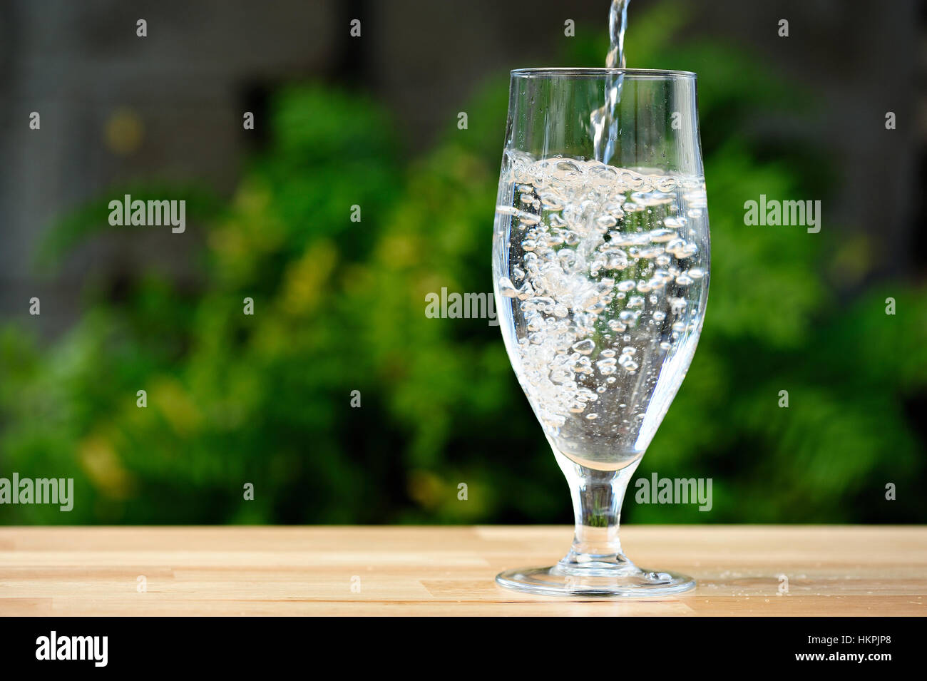 Versare acqua nel bicchiere alto sulla gamba in giardino verde Foto Stock