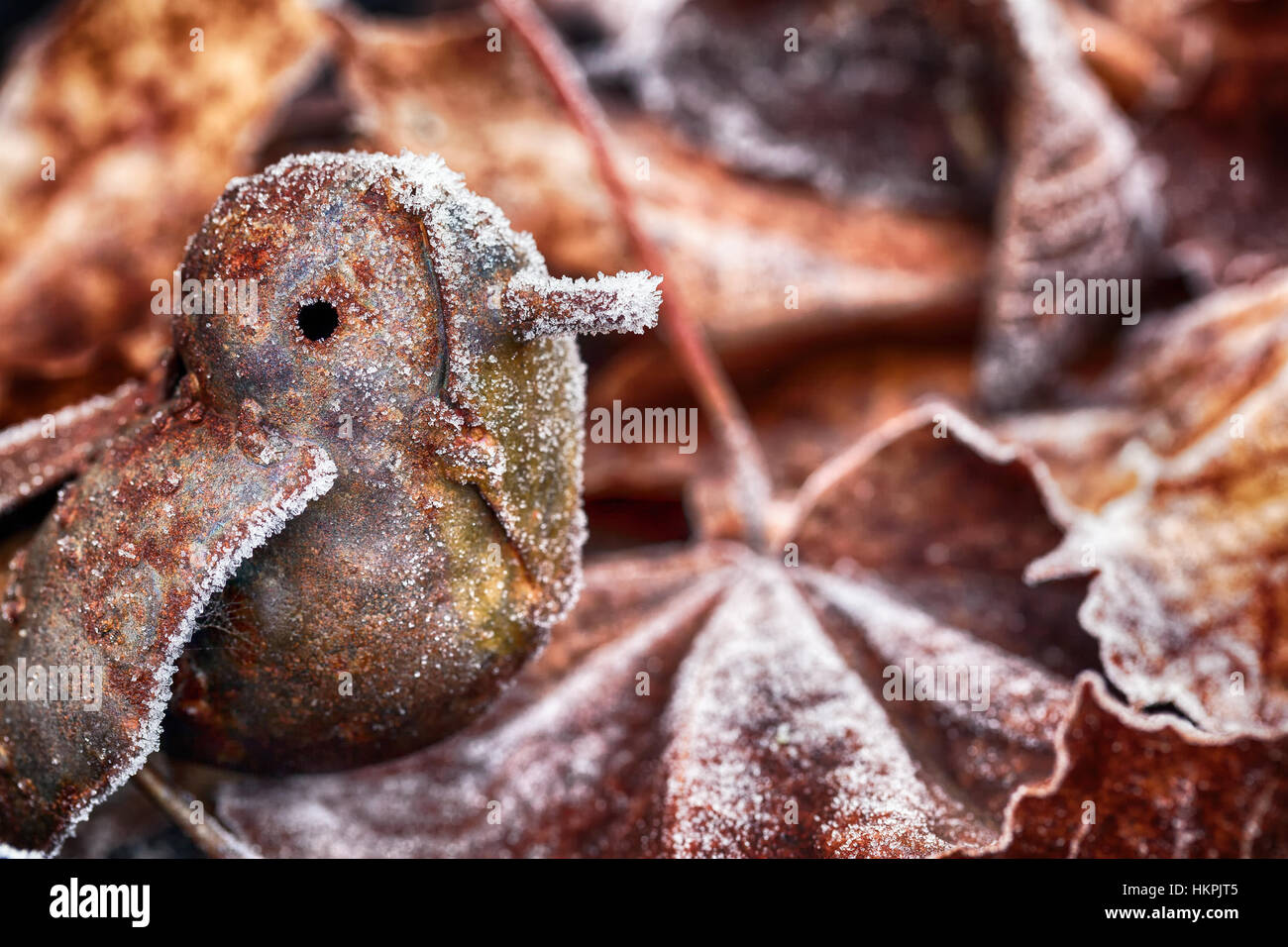 Carino il pupazzo di neve piccolo uccello di metallo tra le foglie congelate di inverno Foto Stock