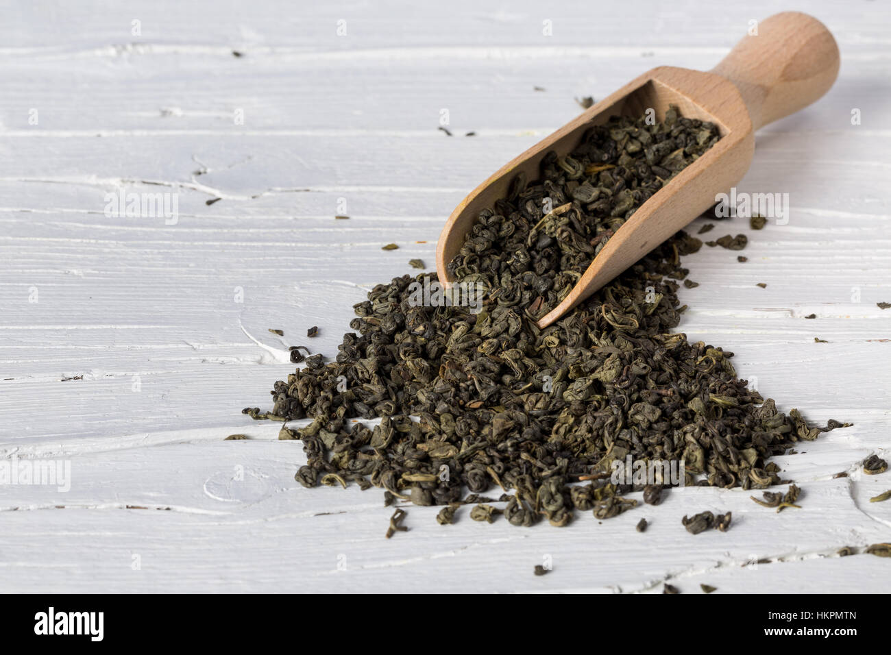 Essiccato Verde foglie di tè con scoop su bianco sullo sfondo di legno, closeup con copia spazio. Foto Stock