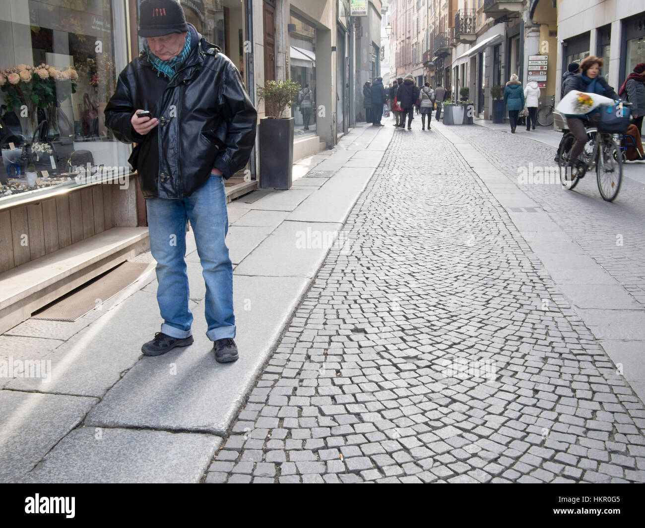 Un vecchio uomo la lettura di un messaggio di testo sul proprio telefono cellulare in strada Foto Stock
