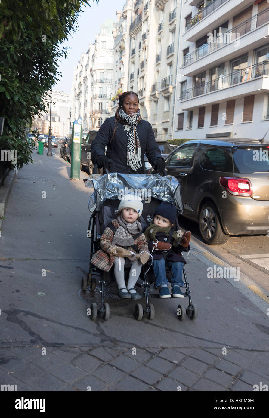 Bambino nero-minder con due bambini bianchi nel passeggino, Auteuil, Parigi, Francia. Foto Stock