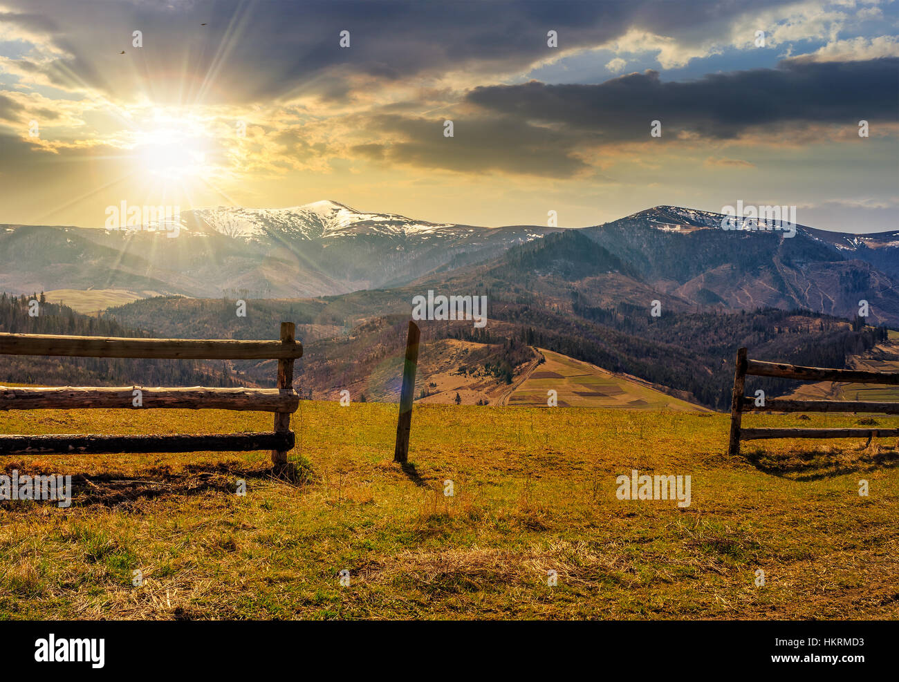 Staccionata in legno sul pendio erboso vicino alle montagne con cime innevate in primavera luce della sera Foto Stock
