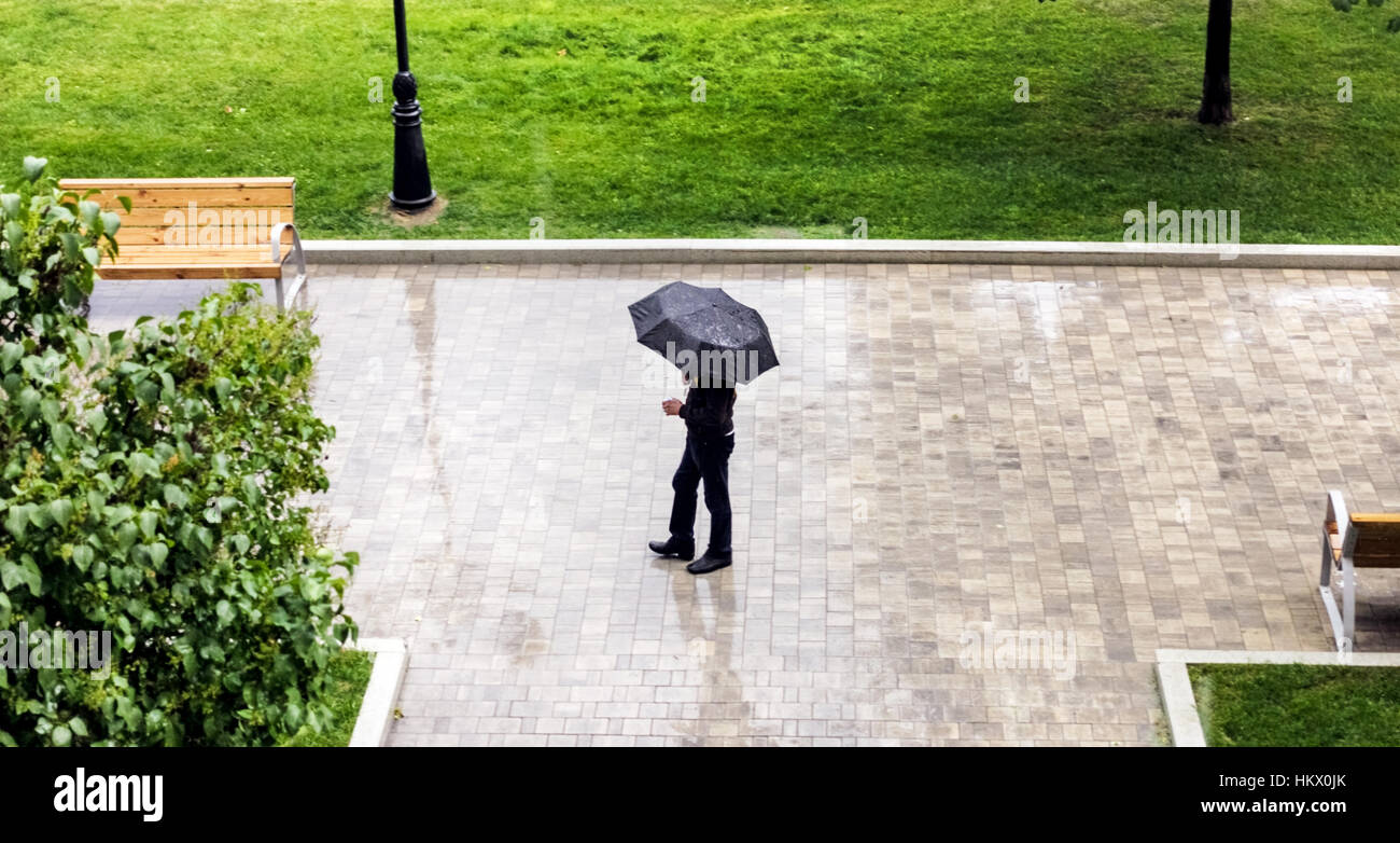 Uomo sotto l'Ombrello nero in estate piovosa meteo in posizione di parcheggio Foto Stock