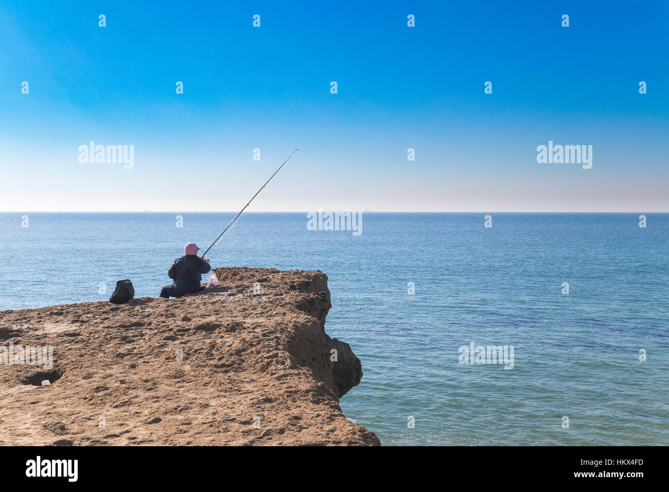 Vecchia persona la pesca nel bordo dell'oceano sulla sommità della roccia sedemenary Foto Stock