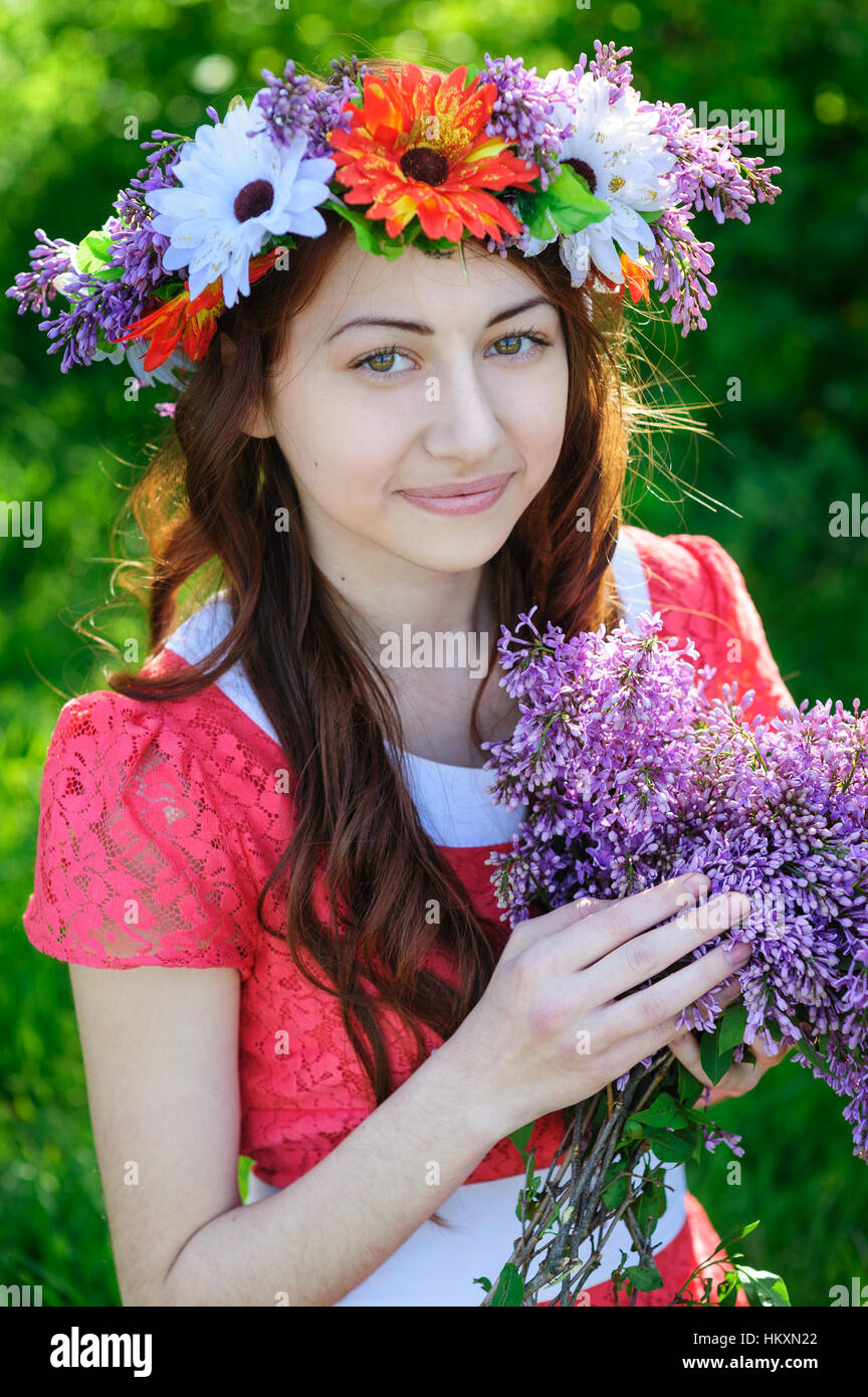 Bella giovane donna con una corona di fiori alla sua testa e mazzo di lillà Foto Stock